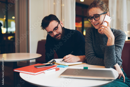 Hipster girl holding book while guy sitting near with smartphone in hand