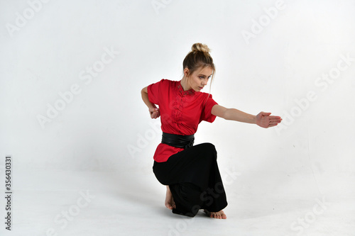 beautiful girl in a red-black suit does exercises in the style of martial arts
