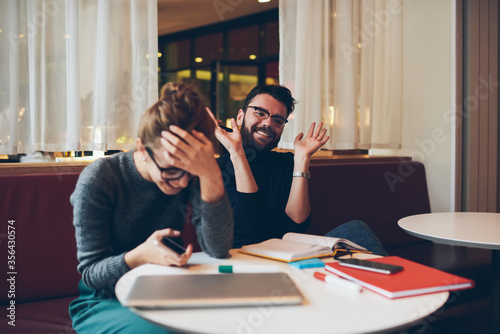 Hipster girl holding book while guy sitting near with smartphone in hand