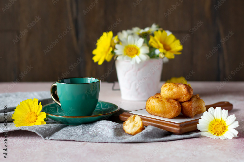 Small sponge biscuits, traditional French madeleines cakes with cup of tea, white and yellow garden flowers on the table. Breakfast or tea time concept