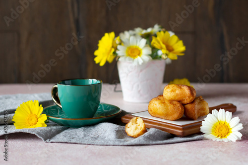 Small sponge biscuits, traditional French madeleines cakes with cup of tea, white and yellow garden flowers on the table. Breakfast or tea time concept