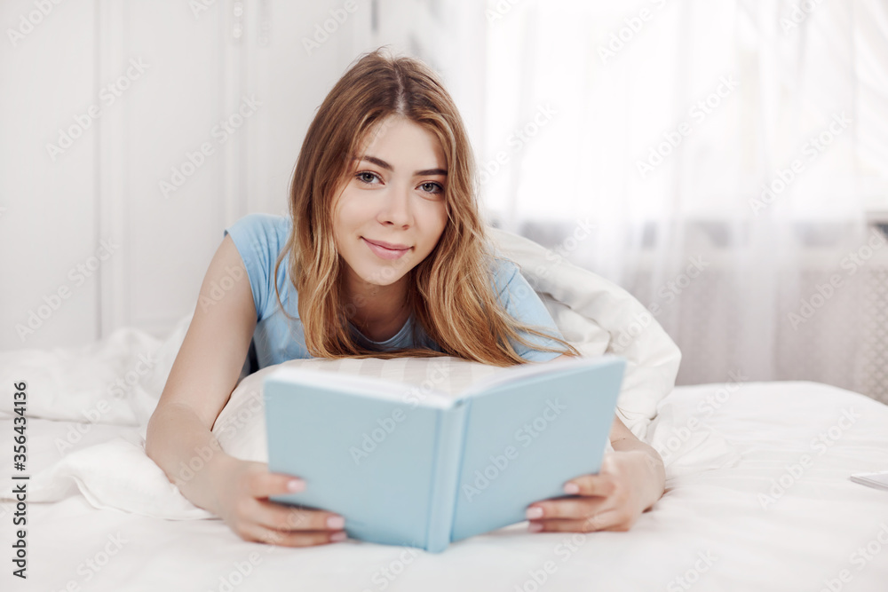 Beautiful girl in blue pajamas reading a book, lying on the bed in the bedroom. Training, education, Hobbies. Beautiful girl in blue pajamas reading a book, lying on the bed in the bedroom. Training, education, Hobbies.