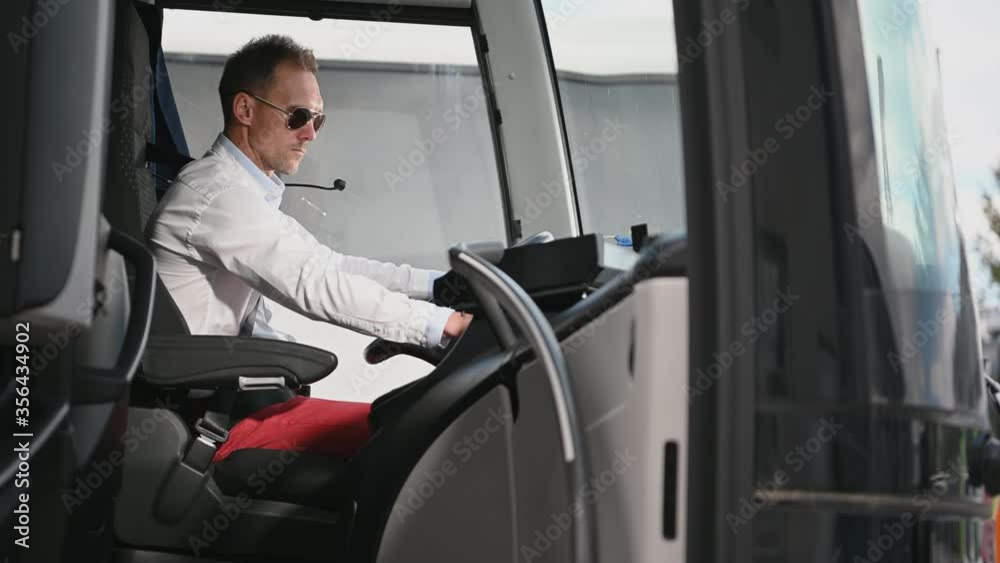 Caucasian Male Bus Driver Checking And Adjusting Knobs And Gages On Dashboard In Vehicle Cabin. Caucasian Male Bus Driver Checking And Adjusting Knobs And Gages On Dashboard In Vehicle Cabin.