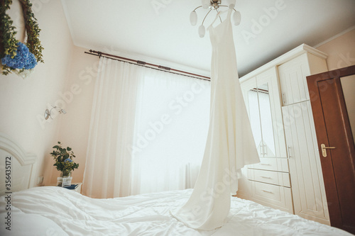 Luxury wedding dress hanging on the chandelier in a hotel room. Bridal gown. Bridesmaids. Wedding