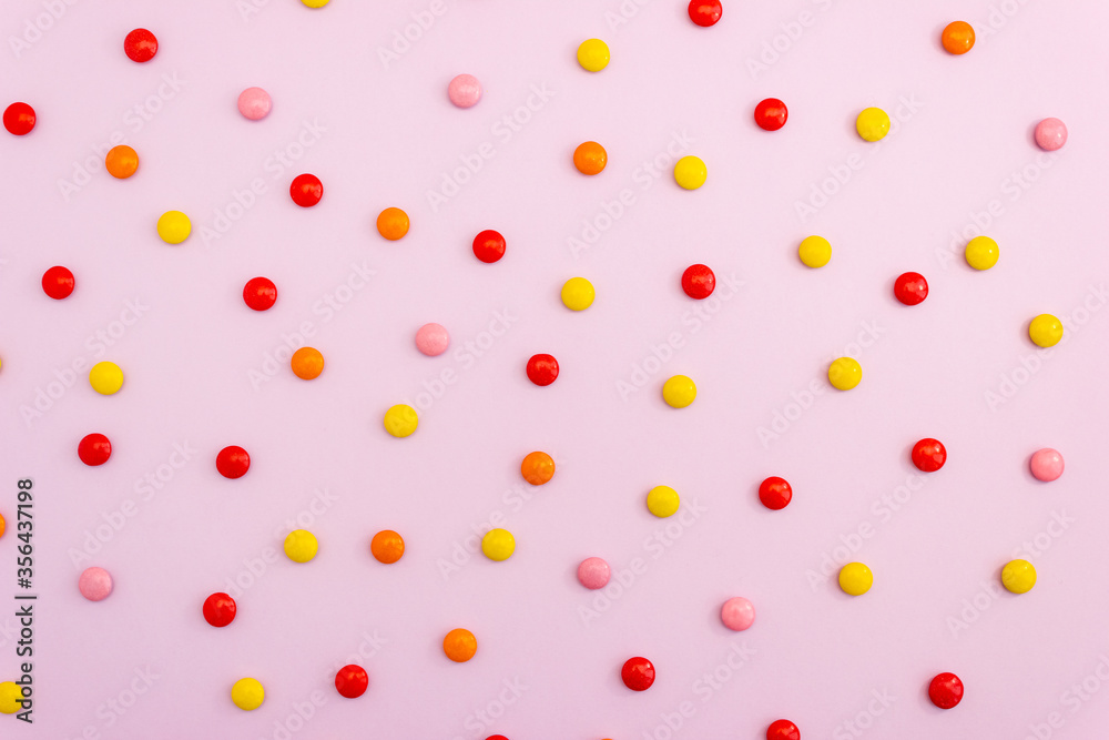 Polka dot pattern made of multicolored chocolate candies on a pink background. Top view, layout. Polka dot pattern made of multicolored chocolate candies on a pink background. Top view, layout.