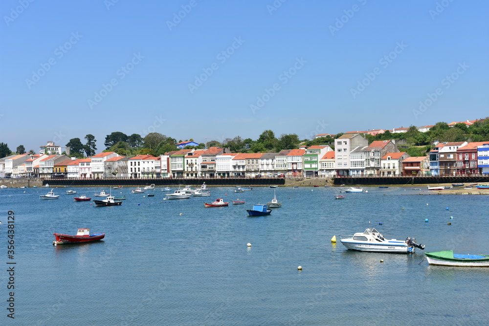 Fishing village with wooden boardwalk, colorful houses and boats with blue sky. Mugardos, Galicia, Spain.