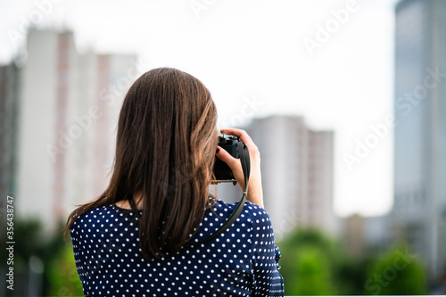 Young woman taking photos with vintage camera outdoors in the city