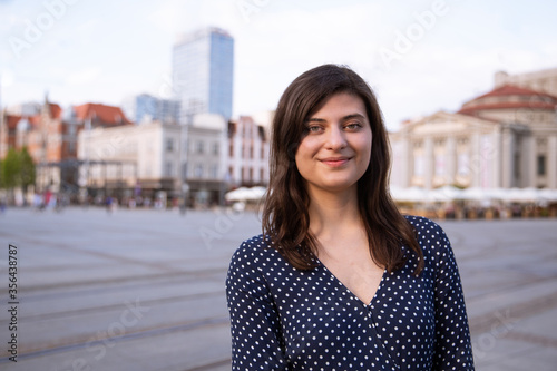 Beautiful young woman standing in the city and smiling gently at camera