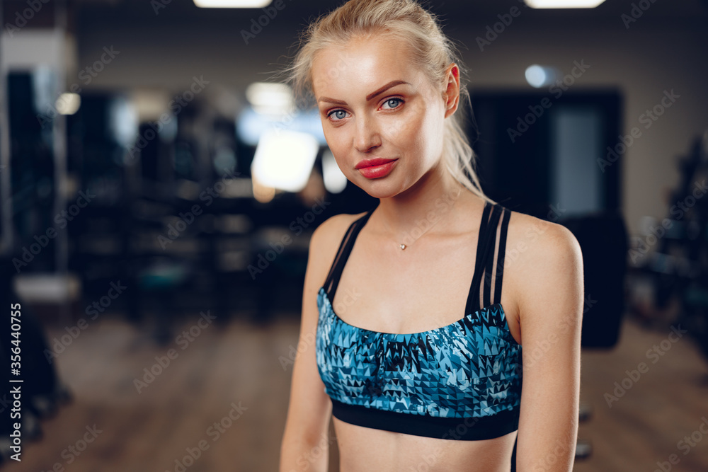 Blonde slim fit woman in sport wear in a dark gym