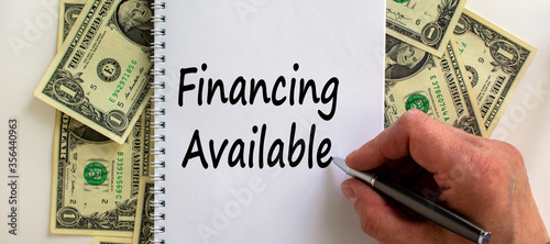 Male hand writing 'financing available' on white note, on white background. Dollar bills. Business concept.