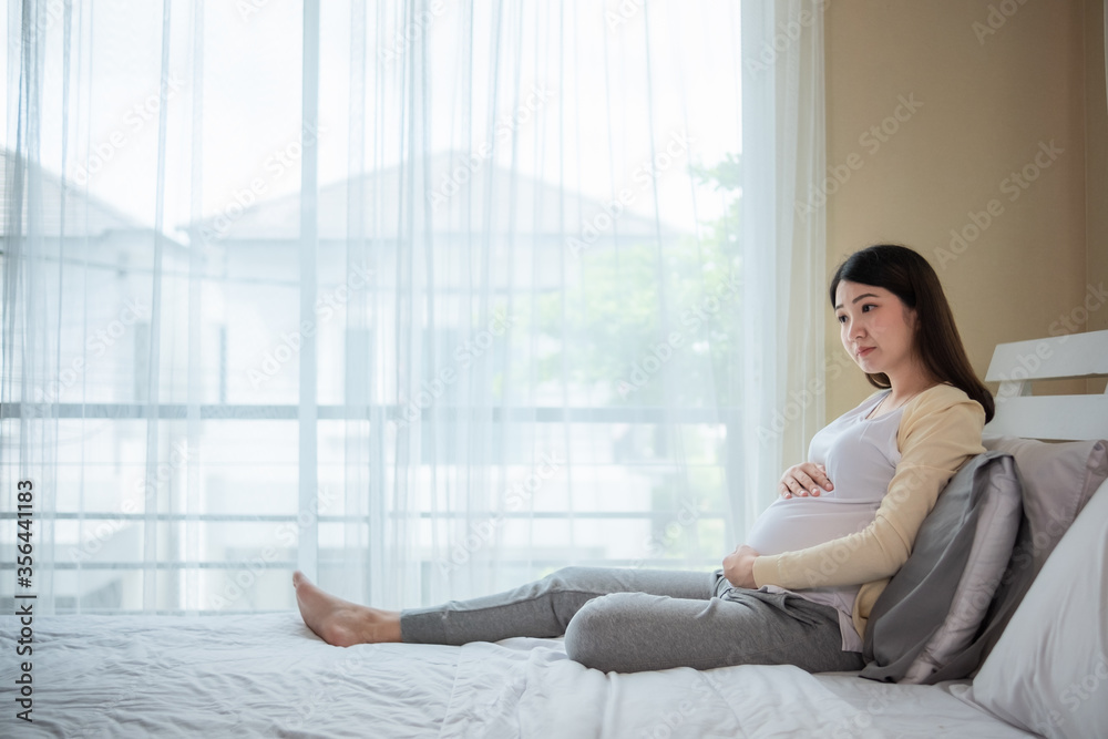 Mom waiting and expecting baby has good health Happy pregnant young asian woman touching abdomen and admiring baby or fetus on bed with happiness smile face. Asia pregnancy mother love baby so much. 