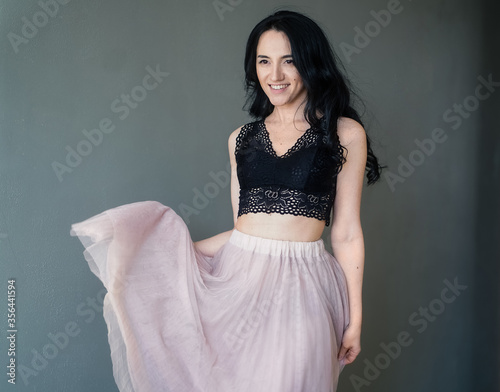 beautiful happy girl in a black top and pink skirt against the gray walls