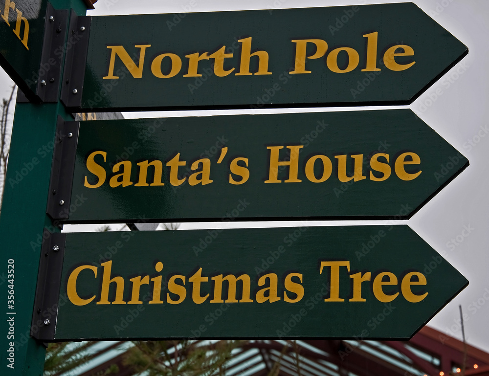 This green Christmas sign post says North Pole, Santa's House, and Christmas Tree for a holiday image.