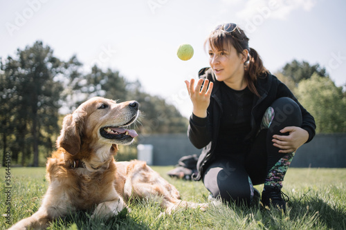 Tableau sur toile Blurred woman throwing ball while squatting next to dog in park