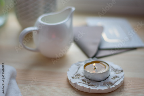 Coffee at home, comfort at home. Milk jug, mug, candlestick, candle, envelope and postcard on wooden desk. White color. Still life a cozy coffee.