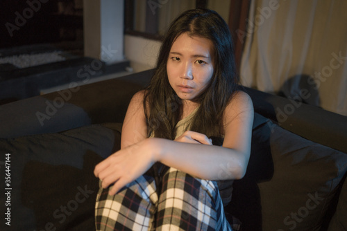 dramatic portrait of young beautiful sad and depressed Asian Korean woman lying in pain at living room sofa couch broken heart suffering depression and anxiety © TheVisualsYouNeed