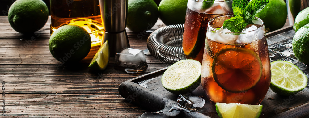 Cuba libre or rum cola cocktail with strong alcohol, lemon juice, lime and ice, dark background, steel bar tools, copy space - obrazy, fototapety, plakaty 