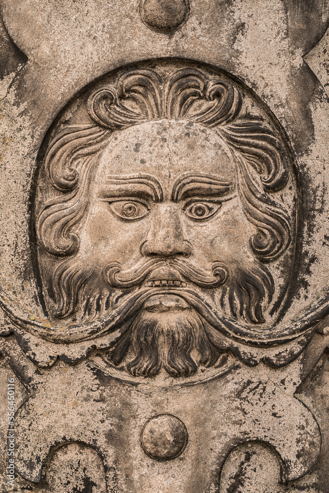 Generic simplified bearded man's face carved from a flat piece of grubby stone shot straight on.