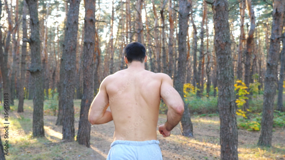 Strong and muscular man running along forest path. Male sportsman working out outdoor. Athletic guy doing cardio training jogging through wood. Concept of healthy active lifestyle. Slow motion Strong and muscular man running along forest path. Male sportsman working out outdoor. Athletic guy doing cardio training jogging through wood. Concept of healthy active lifestyle. Slow motion