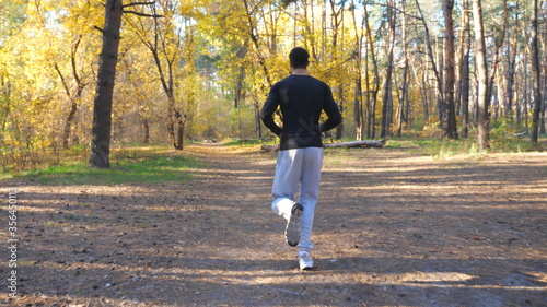 Unrecognizable man running fast along forest path at sunny day. Strong and endurance athlete working out at nature. Sporty guy doing cardio training in scenic wood. Concept of active lifestyle