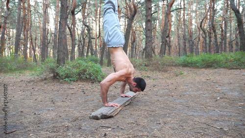 Young muscular man doing push ups in handstand at forest. Hardy and strong guy doing stunts at wood. Athlete showing gymnastic exercises outdoor. Sportive and healthy lifestyle. Slow motion Close up