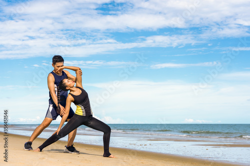 Female athletes train by a male personal coach to stretch before exercising at the sea in summer holiday