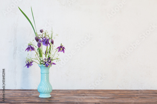 flowers in vase on wooden table on background white wall