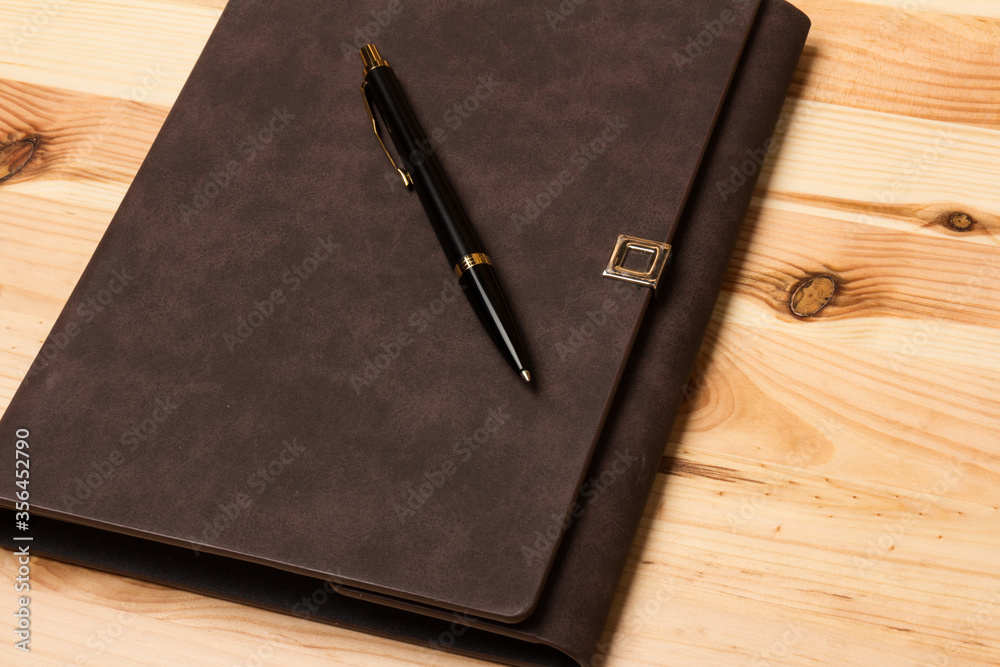 Leather-bound business notebook with a Parker pen on wooden background. Business concept Leather-bound business notebook with a Parker pen on wooden background. Business concept