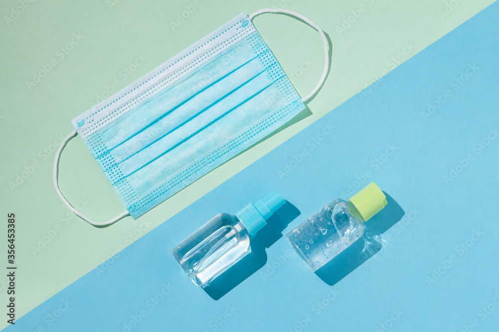 Blue surgical face mask, antibacterial gel and alcohol spray to prevent contagion of corona. Blue and green background Blue surgical face mask, antibacterial gel and alcohol spray to prevent contagion of corona. Blue and green background