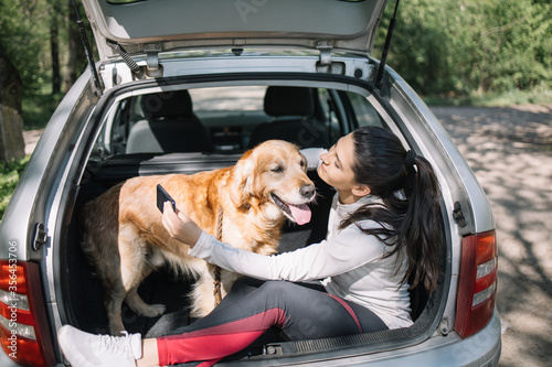 Young woman and dog sitting in car. Dog sitting in opened trunk while girl in sport outfit is hugging him. © Synergic Works OÜ