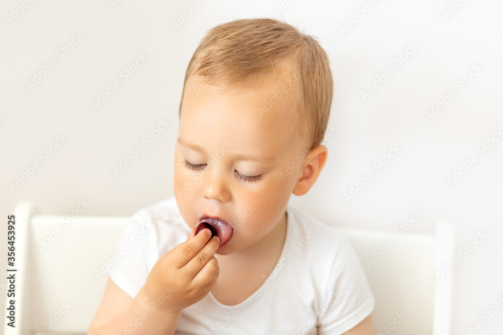 portrait of a baby boy 2 years old on a white isolated background and eating a berry, baby food concept, place for text portrait of a baby boy 2 years old on a white isolated background and eating a berry, baby food concept, place for text