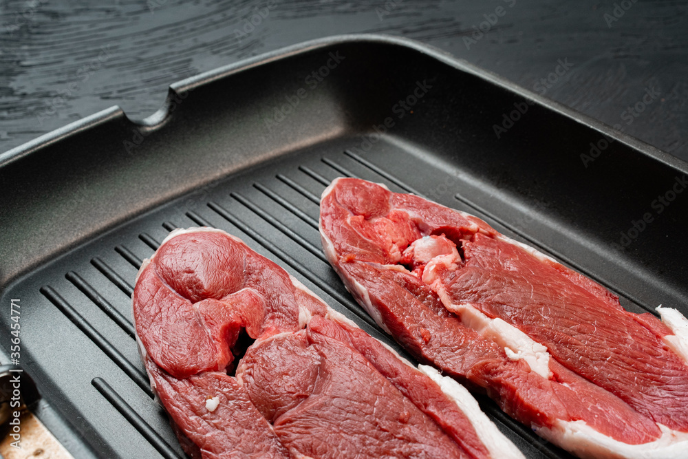 Raw steak on frying grill pan. Dark background.