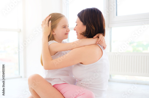 Mother with her little daughter girl tender hugging in white room