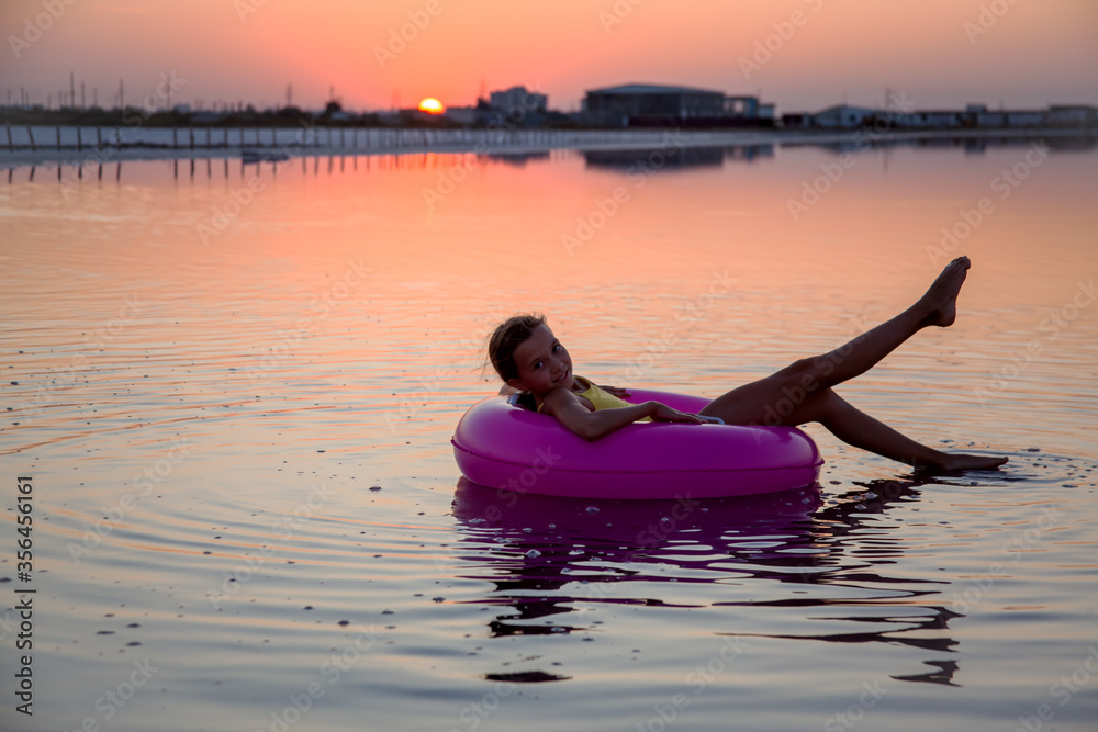 Young girl swimming on ring in the sea or ocean at the background purple sunrise. Female wearing yellow swimsuit. The legs of the model are raised to the top on the summer. Young girl swimming on ring in the sea or ocean at the background purple sunrise. Female wearing yellow swimsuit. The legs of the model are raised to the top on the summer.