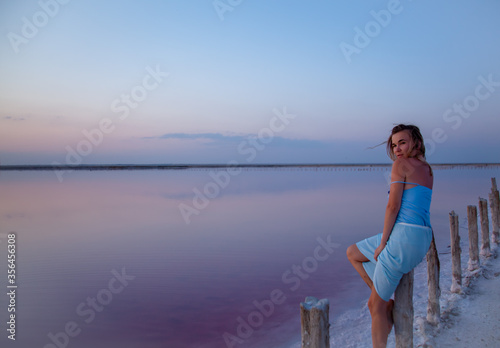 Beautiful sensual woman posing and look to the purple sunrise in water on summer. Woman sit on the shore of the salt beach at pink lake agains blue sky. vacation lifestyle near ocean.
