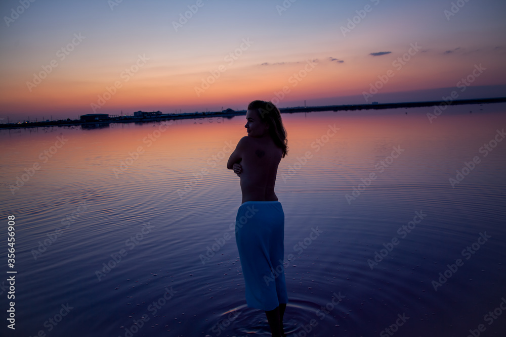 Rear view of the woman nude back silhouette look to the purple sunrise in water on summer. Woman sit on the shore of the salt beach at pink lake. vacation lifestyle near ocean