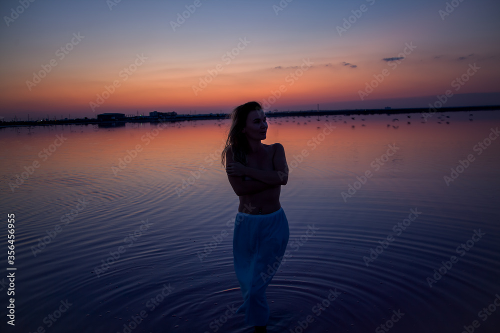 The silhouette of woman look to the purple sunrise in water on summer. Woman sit on the shore of the salt beach at pink lake. vacation lifestyle near ocean