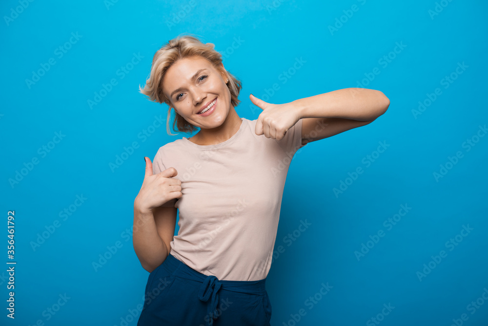 Young blonde woman gesturing the like sign on a blue studio background smiling at camera Young blonde woman gesturing the like sign on a blue studio background smiling at camera