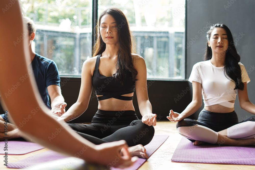 Group of young people in yoga class with trainer making meditation lotus pose on yoga sheet at gym feel relax concentrate and healthy sport activity Group of young people in yoga class with trainer making meditation lotus pose on yoga sheet at gym feel relax concentrate and healthy sport activity