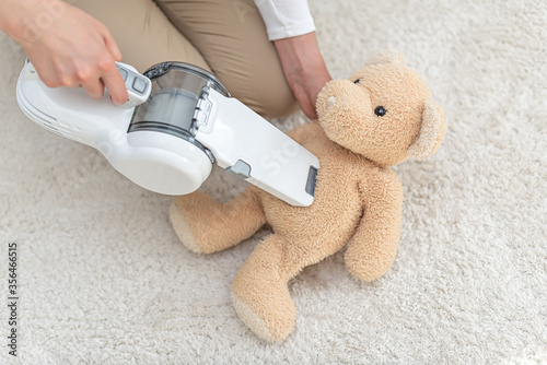 Woman vacuuming furniture in a house with a hand-held portable vacuum cleaner.