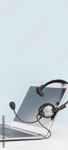 Laptop with blank screen and headphones on desk blue background. copy space. Distant learning or working from home, online courses or cutomer assistance concept. Helpdesk or call center mono headset  photo