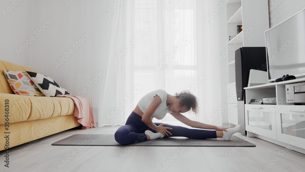 Slim sporty african american woman practicing yoga on a mat. Woman sits on fitness mat and stretches Slim sporty african american woman practicing yoga on a mat. Woman sits on fitness mat and stretches