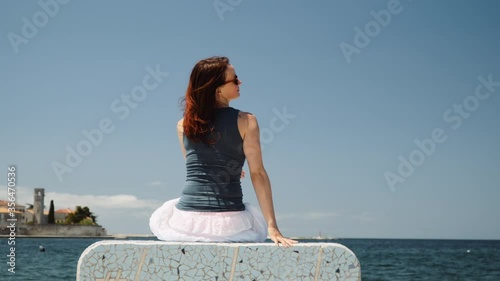 Caucasian woman sitting on the stone bench, sea and old town in background.