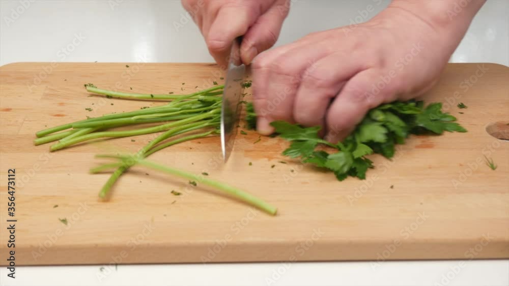 A man finely cuts parsley with a Japanese knife santoku, hands, close-up A man finely cuts parsley with a Japanese knife santoku, hands, close-up