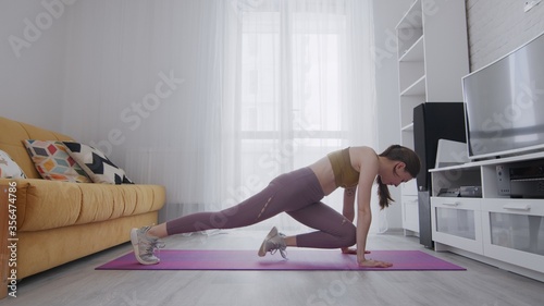 Portrait of a beautiful slim sporty woman practicing yoga on a mat. Woman doing sports exercises rock climber at home