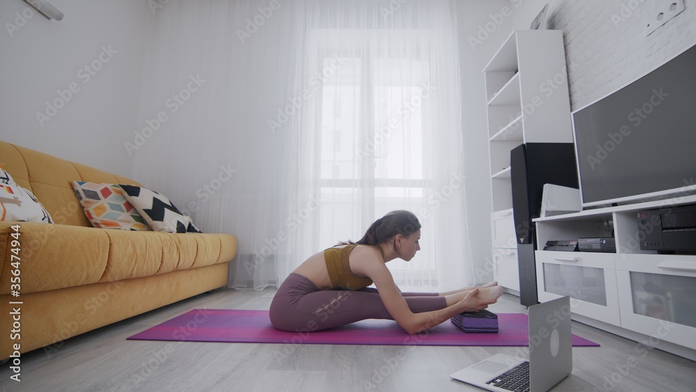 On-line work out woman using internet services with help of her instructor. Portrait of a beautiful slim sporty woman practicing yoga on a mat. Woman doing stretching exercises on violet mat at home On-line work out woman using internet services with help of her instructor. Portrait of a beautiful slim sporty woman practicing yoga on a mat. Woman doing stretching exercises on violet mat at home