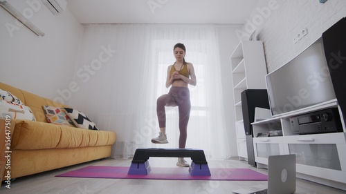 On-line work out woman using internet services with help of her instructor. Slim woman stepping on a step platform