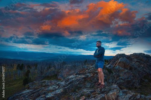 Travel, freedom and tourism concept - man standing on top of cliff in summer beauty evening in Altai mountains, fantastic sunset