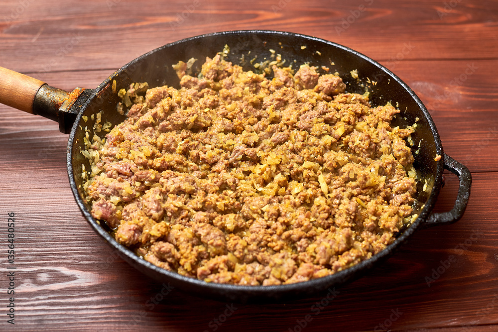 Grilled minced meat with onions, spices and cream in a pan on a dark wooden background. Cooking toppings. Grilled minced meat with onions, spices and cream in a pan on a dark wooden background. Cooking toppings.