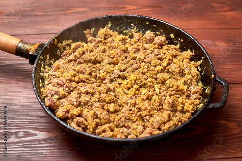 Grilled minced meat with onions, spices and cream in a pan on a dark wooden background. Cooking toppings.